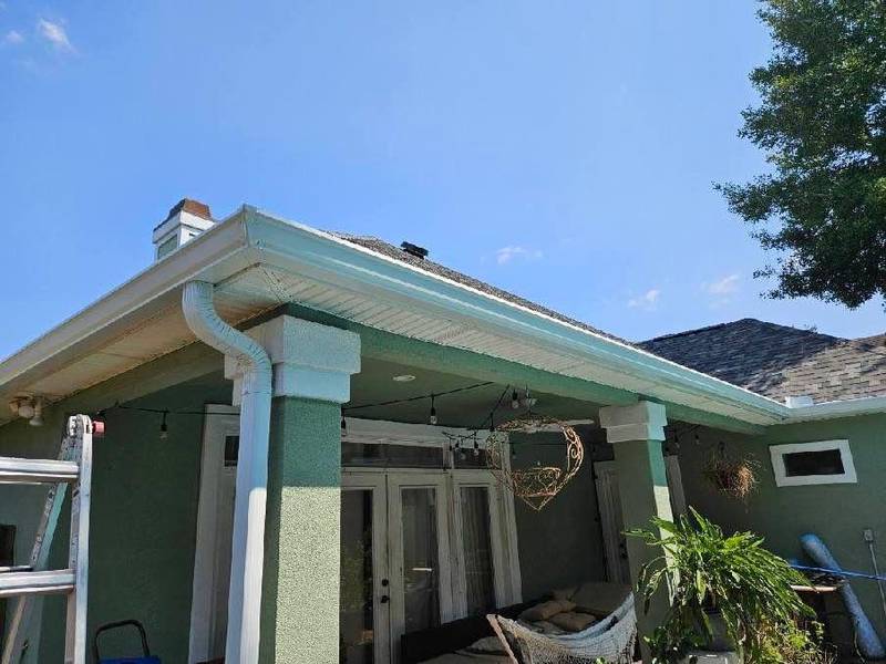 Back porch of a green house with new white gutters and a downspout