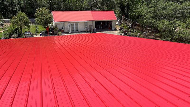 Bright red ribbed metal roof seen from the ridge, with a red-roofed outbuilding behind